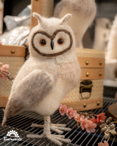 Décoration hibou en peluche devant des boîtes en bois et fleurs.
